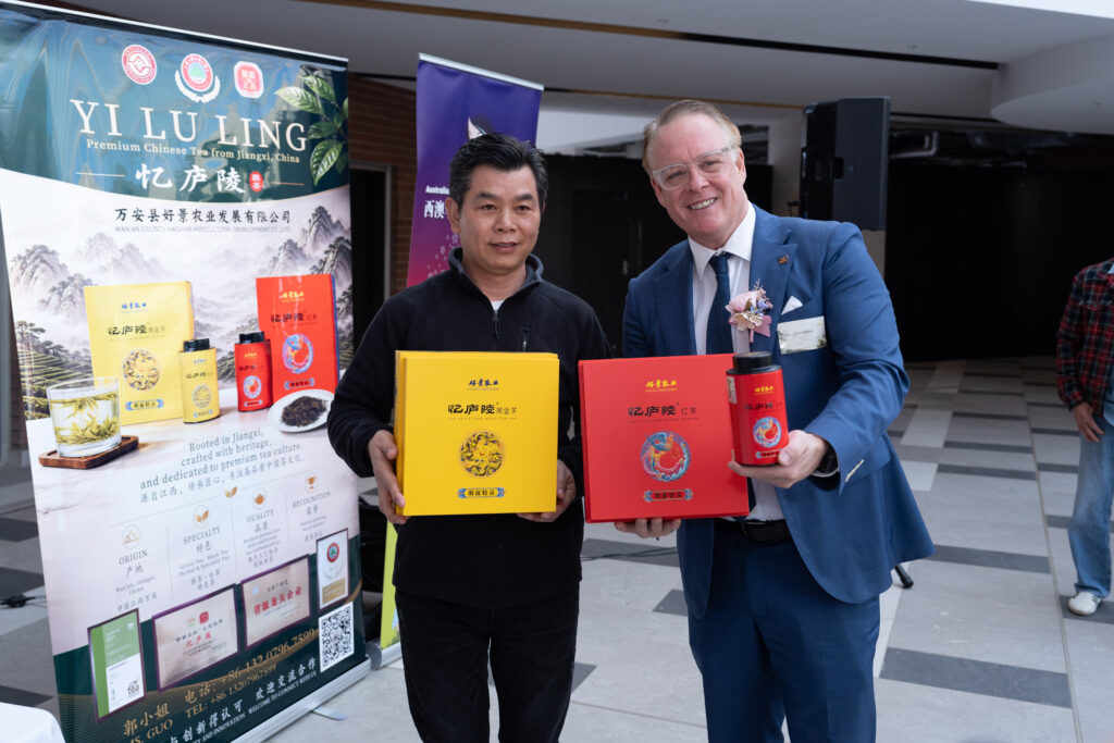 Two men holding Yi Lu Ling tea gift boxes beside a Yi Lu Ling banner at a product showcase